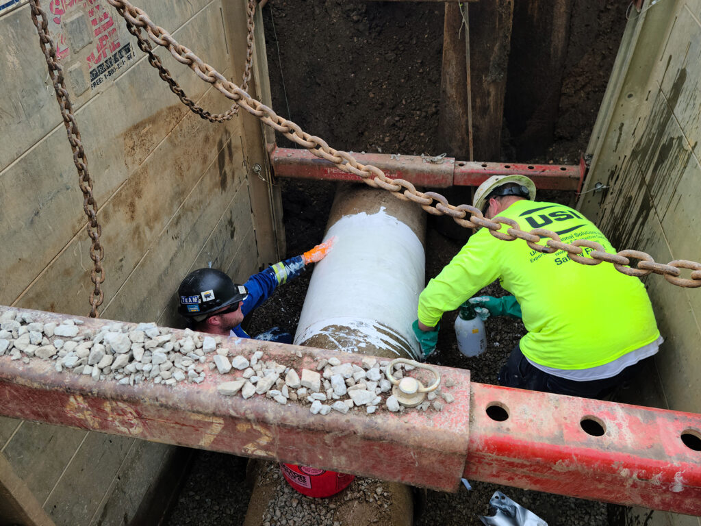 A USI expert helps put the final coating on the pipe that is being repaired. 